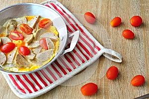 Breakfast with fried eggs in a pan with white pork sausage, tomato, fork on a wooden background