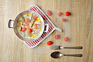 Breakfast with fried eggs in a pan with white pork sausage, tomato, fork on a wooden background