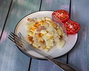 Breakfast of fried potatoes and red tomato cut in half on a light ceramic plate