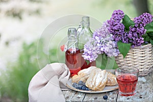 Breakfast in the garden: eclairs, cup of coffee, coffee pot, lilac flowers in a basket