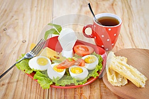 Breakfast with hard boiled eggs, sliced in halves, cup of tea, salad, tomatoes, cheese and bread on the red plate