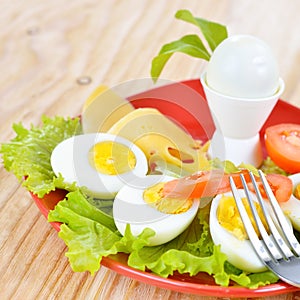 Breakfast with hard boiled eggs, sliced in halves, salad, tomatoes and cheese on the red plate