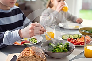 Breakfast at home: children drinking orange juice and nailing fresh green broccoli on a fork