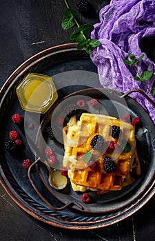 Breakfast. Homemade belgian waffles with berries and honey on dark table.