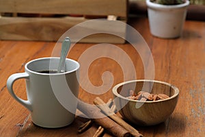 Breakfast hot black coffee in white cup, cinnamon, almond nut in wooden bowl and cactus pot plant on wood table