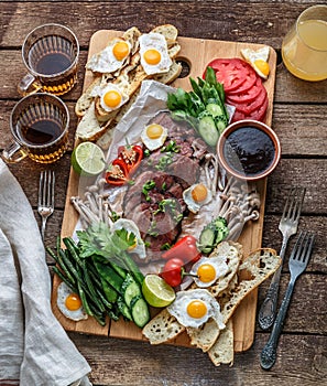 Breakfast meals variety flat lay. Top view on buffet wooden board with meat, eggs, vegetables, bread etc