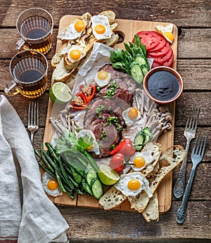 Breakfast meals variety flat lay. Top view on buffet wooden board with meat, eggs, vegetables, bread etc