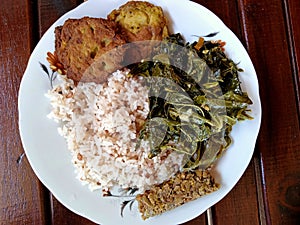 The breakfast menu on a plate consists of rice, steamed pork, potato cakes and cassava leaves