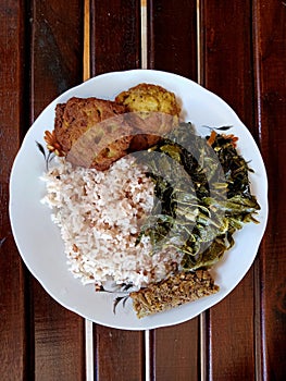 The breakfast menu on a plate consists of rice, steamed pork, potato cakes and cassava leaves