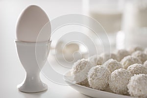 Breakfast - milk, eggs, cream cheese and raffaello coconut confectionery on white wood table. white on white picture.