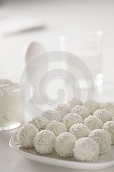 Breakfast - milk, eggs, cream cheese and raffaello coconut confectionery on white wood table. white on white picture.