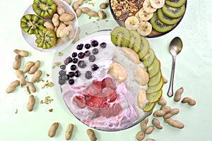 Breakfast with muesli, acai blueberry smoothie and kiwi, fruits on green background. Healthy food concept. Flat lay, top vie
