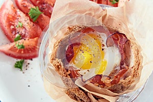 Breakfast muffin from egg and bacon in toasted bread, tomato and