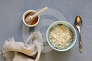 Breakfast of oatmeal porridge in a blue bowl, honey in a white bowl with a wooden honey spoon and a cloth napkin, silver spoon on