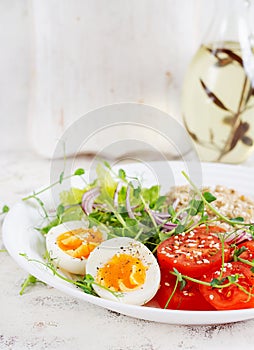 Breakfast oatmeal porridge with boiled eggs and fresh vegetables.