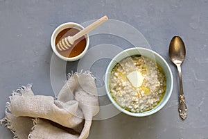 Breakfast of oatmeal porridge and butter in a blue bowl, honey in a white bowl with a wooden honey spoon and a cloth napkin,