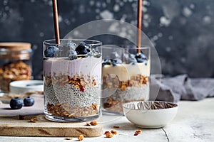 Breakfast parfait with chia, granola, berries and yogurt in a glass, dark background. Layer dessert in glass