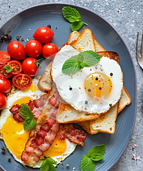 A breakfast plate with French toast, fried egg and bacon garnished with fresh mint leaves and cherry tomatoes