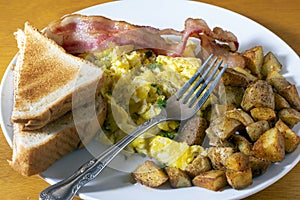 breakfast plate of scramble eggs and bacon with homefries