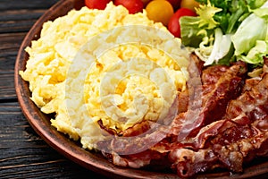 Breakfast plate . Scrambled eggs , bacon , cherry tomatoes and salad