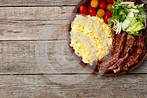 Breakfast plate . Scrambled eggs , bacon , cherry tomatoes and salad
