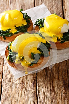 Breakfast of poached eggs with spinach and hollandaise sauce on bread close-up. vertical