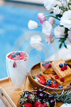 Breakfast by the pool with fruits and berries in wooden bowls: waffles, milkshake, strawberries, raspberries, blueberries,