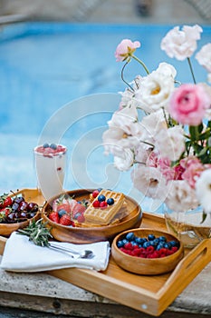 Breakfast by the pool with fruits and berries in wooden bowls: waffles, milkshake, strawberries, raspberries, blueberries,