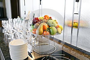 Breakfast in restaurant of hotel. Plate with fruits and berries on a smorgasbord. Many wineglasses. in the background