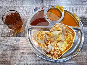 Breakfast a roti canai telur or egg bread with sauces and glass of tea on wooden background