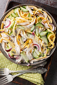 Breakfast salad of shredded chicken, cucumber, red onion and chopped egg pancakes closeup on the plate. Vertical top view