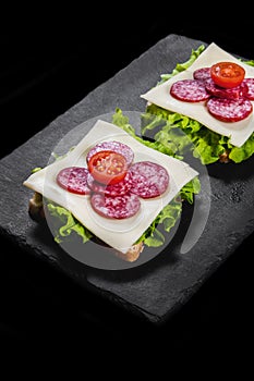 Breakfast sandwiches with dry meat, cheese and lettuce on a black plate