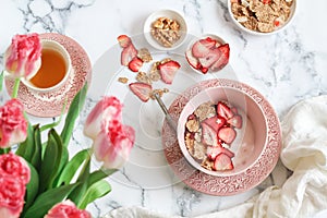 Breakfast scene with yogurt, granola and dried strawberries bowl and a cup of tea on a mable table