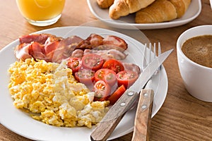 Breakfast with scrambled eggs, bacon, tomatoes,coffee,orange juice ,croissant and corn flakes