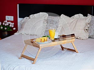 Breakfast served in bed on a wooden tray with tea, juice, cookies. Hotel room service, relax concept