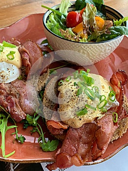 breakfast set, eggs benedict on toast, bacon, salad in a bowl, brown bread, spilled eggs