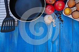 Breakfast Set. Frying pan, tomatoes, raw eggs, onions, garlic, spices. Selective focus. Copy space. Top view. On blue wooden