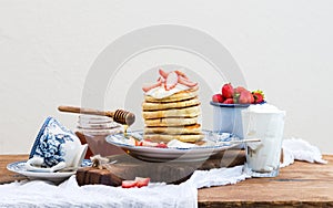 Breakfast set. Pancake tower with fresh strawberries, sour cream and honey on a porcelain plate over rustic wooden table