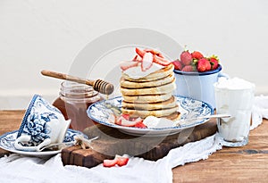 Breakfast set. Pancakes with fresh strawberries, sour cream and honey on a porcelain plate over rustic wooden table