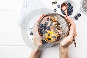 Breakfast smoothie bowl with chia pudding, berries and granola in a coconut shell on white wooden background