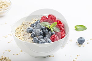 Breakfast smoothie bowl with granola, fresh raspberries, blueberries and mint on white background. Healthy food.