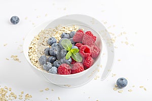 Breakfast smoothie bowl with granola, fresh raspberries, blueberries and mint on white background. Healthy food.