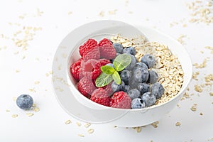 Breakfast smoothie bowl with granola, fresh raspberries, blueberries and mint on white background. Healthy food.