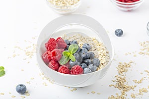 Breakfast smoothie bowl with granola, fresh raspberries, blueberries and mint on white background. Healthy food.