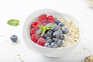 Breakfast smoothie bowl with granola, fresh raspberries, blueberries and mint on white background. Healthy food.