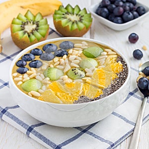 Breakfast smoothie bowl with matcha green tea, kiwi, banana and almond milk, topped with berries, fruits, nuts and seeds, square