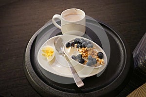 A breakfast snack of an hardboiled egg, yogurt, blueberries and cappuccino at an airport lounge