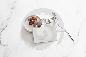 Breakfast, snack still life scene. Blank business card mock-up. Red fresh grapes fruit on ceramic plate and olive tree