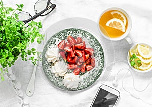 Breakfast or snack table - fresh strawberries, meringue, green tea with lemon, smartphone and headphones. Cozy home rest break sti