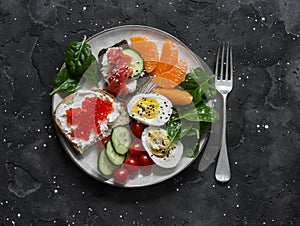 Breakfast, snack, tapas plate - sandwiches with red caviar, salmon, cream cheese, vegetables, spinach, boiled egg on a dark